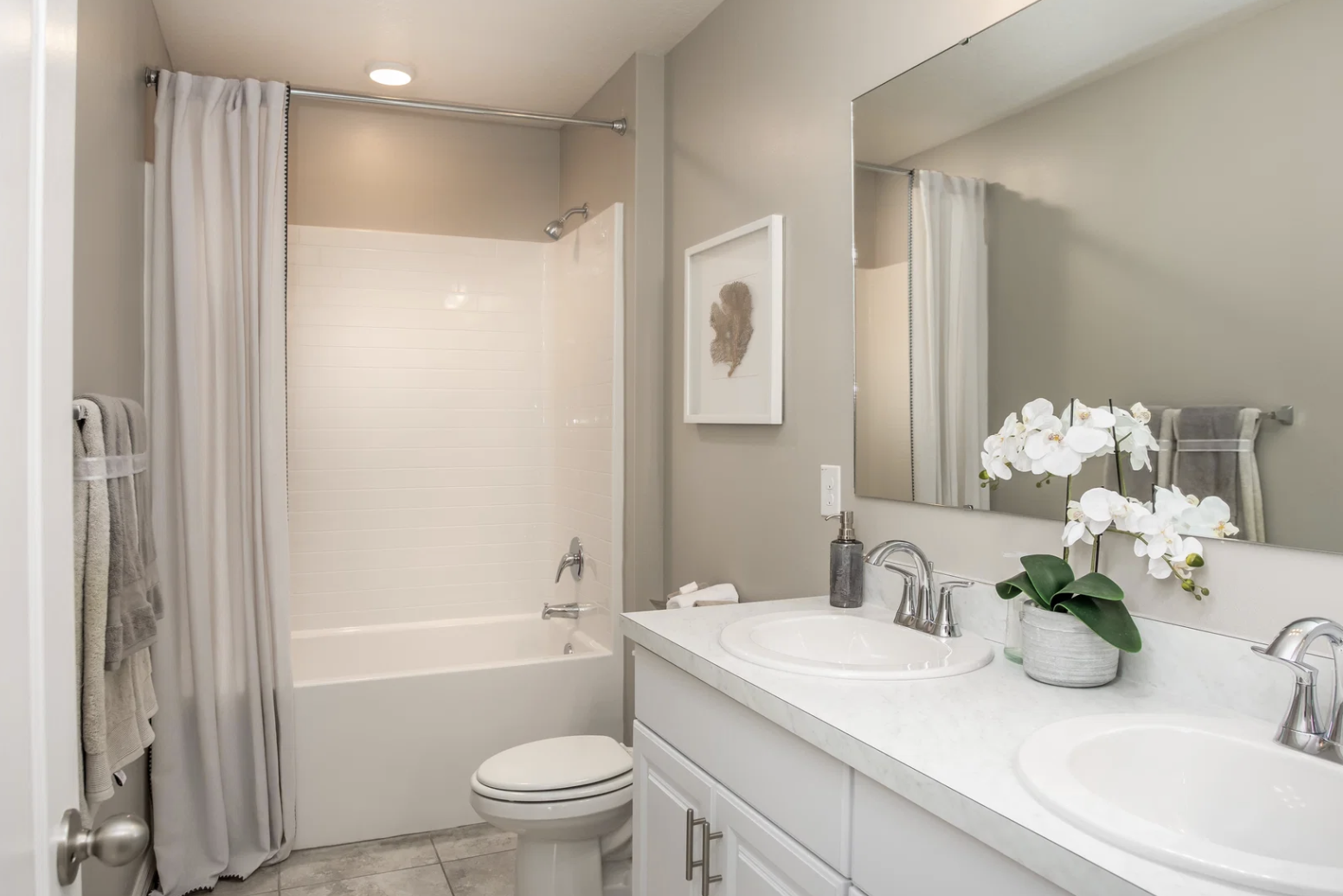 Modern bathroom featuring a bathtub, double sink vanity with white countertops, and decorative orchid plant.