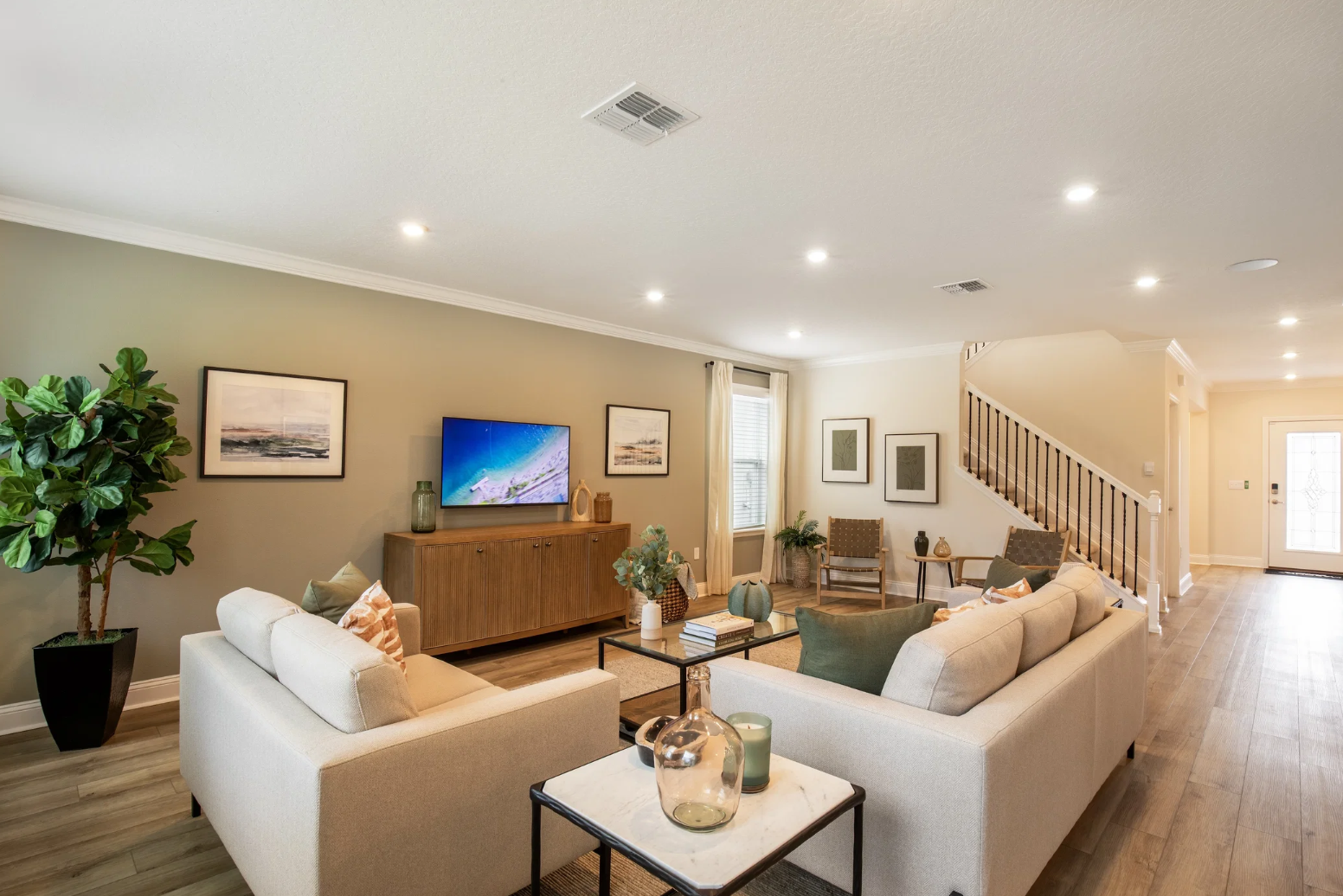 A modern living room with light-colored furniture, a television on the wall, and a decorative plant.