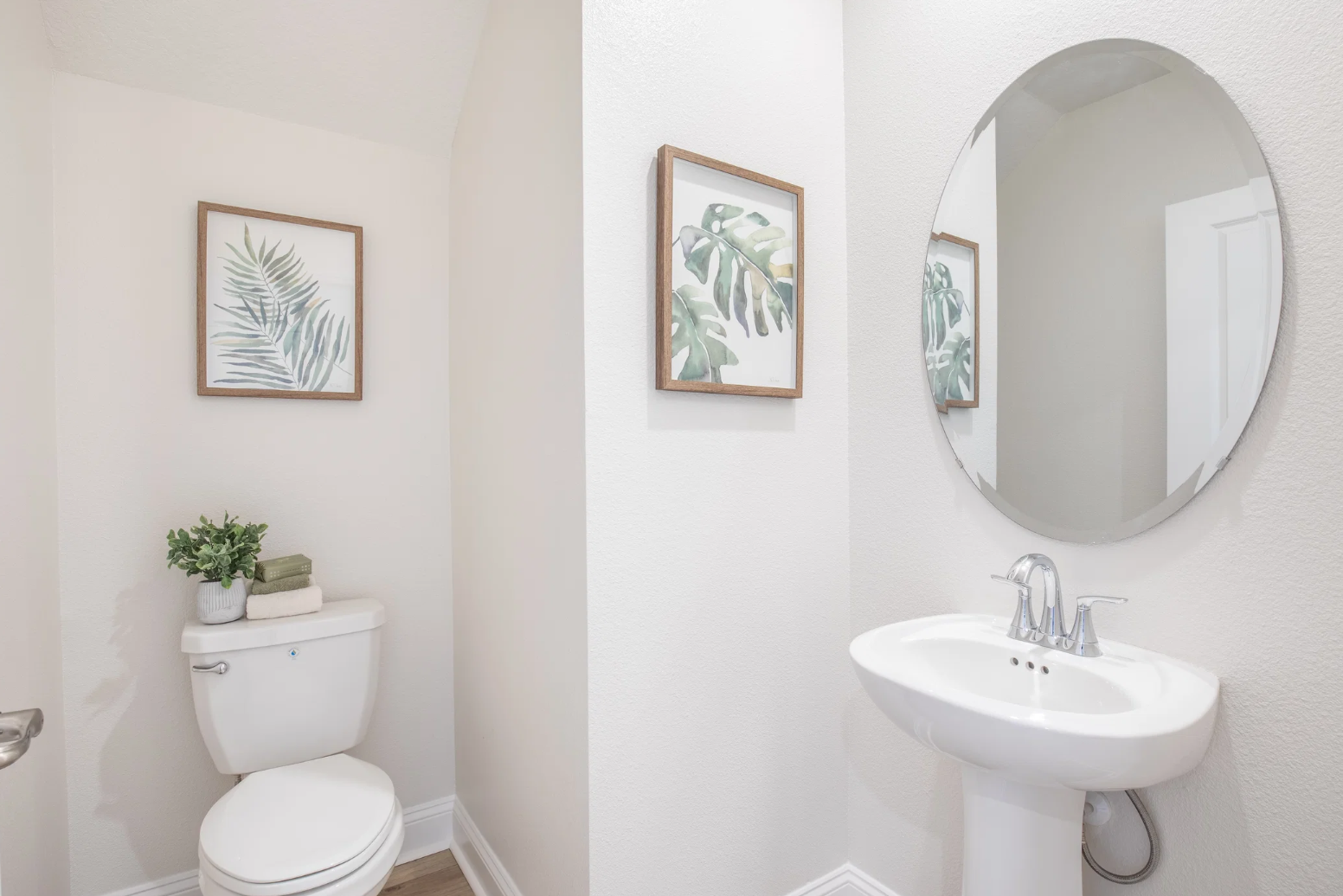 A stylish and modern bathroom featuring a white toilet, a circular mirror, and framed botanical artwork on the walls.