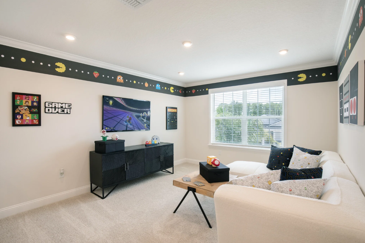 A stylish game room featuring retro video game decor, modern furniture, and bright natural light from large windows.