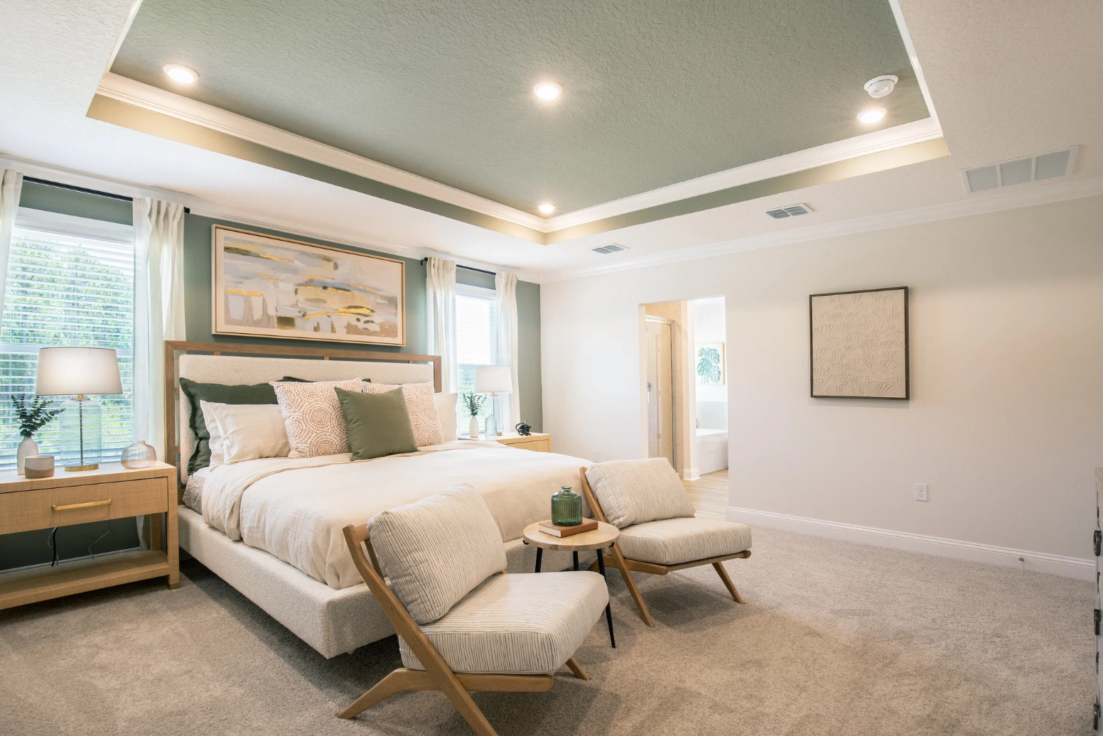 A modern bedroom featuring a large bed, two accent chairs, and large windows with natural light.