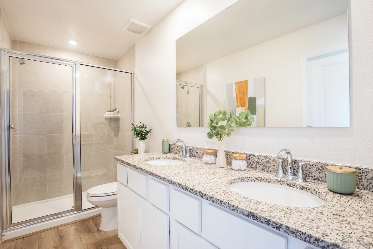 Modern bathroom featuring a double sink vanity with granite countertops, a glass shower, and elegant decor.