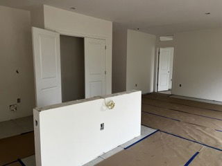 A partially constructed interior room with white walls, open doorways, and floor protection in a new building.