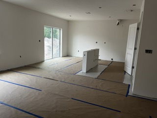 Empty modern room under renovation with hardwood floors covered for protection and a large glass sliding door.