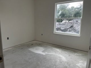 Empty room with bare floor, white walls, and a window overlooking a construction site.