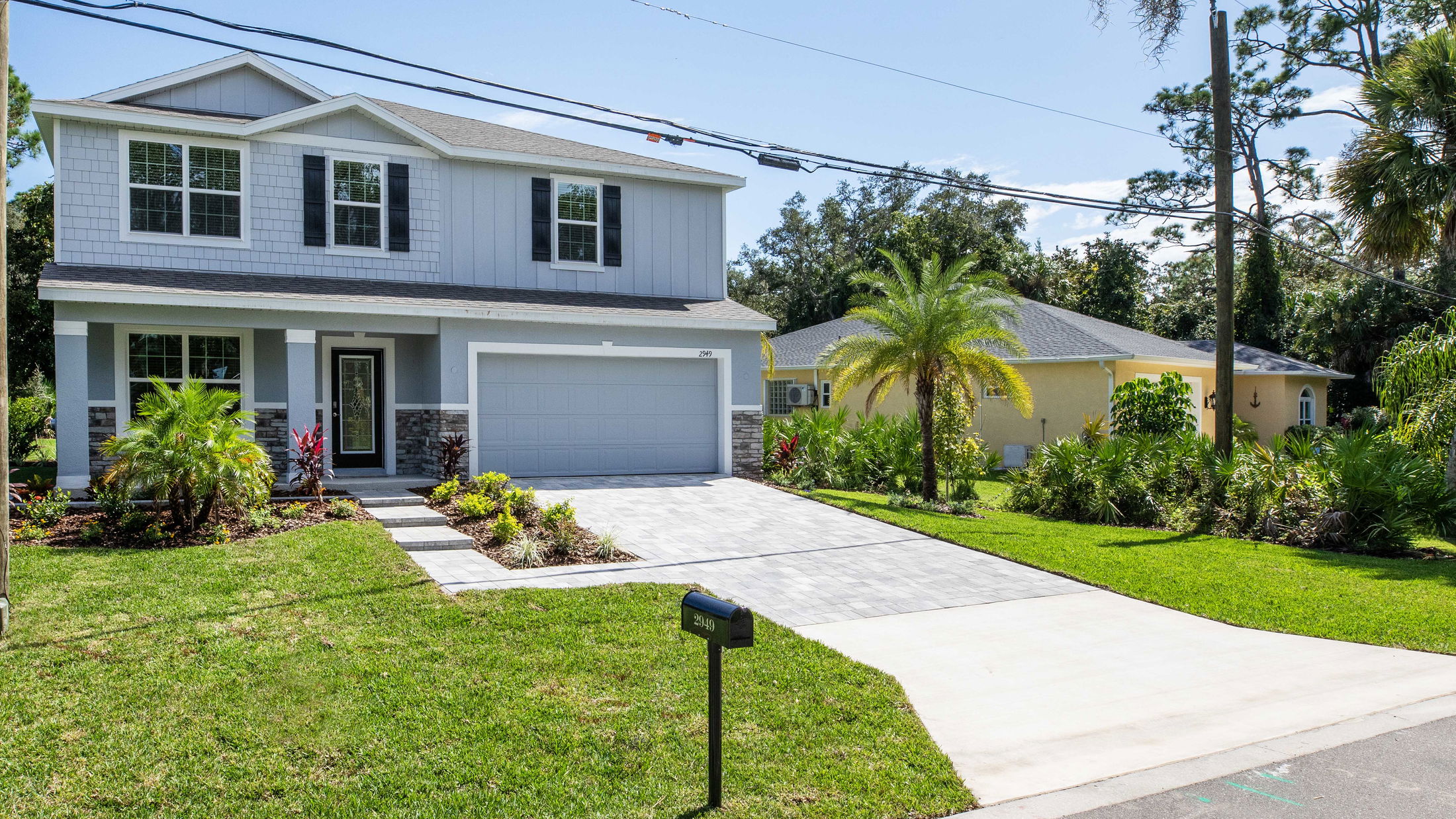 Two-story modern house with a garage, landscaped front yard, and palm trees, viewed from the street.