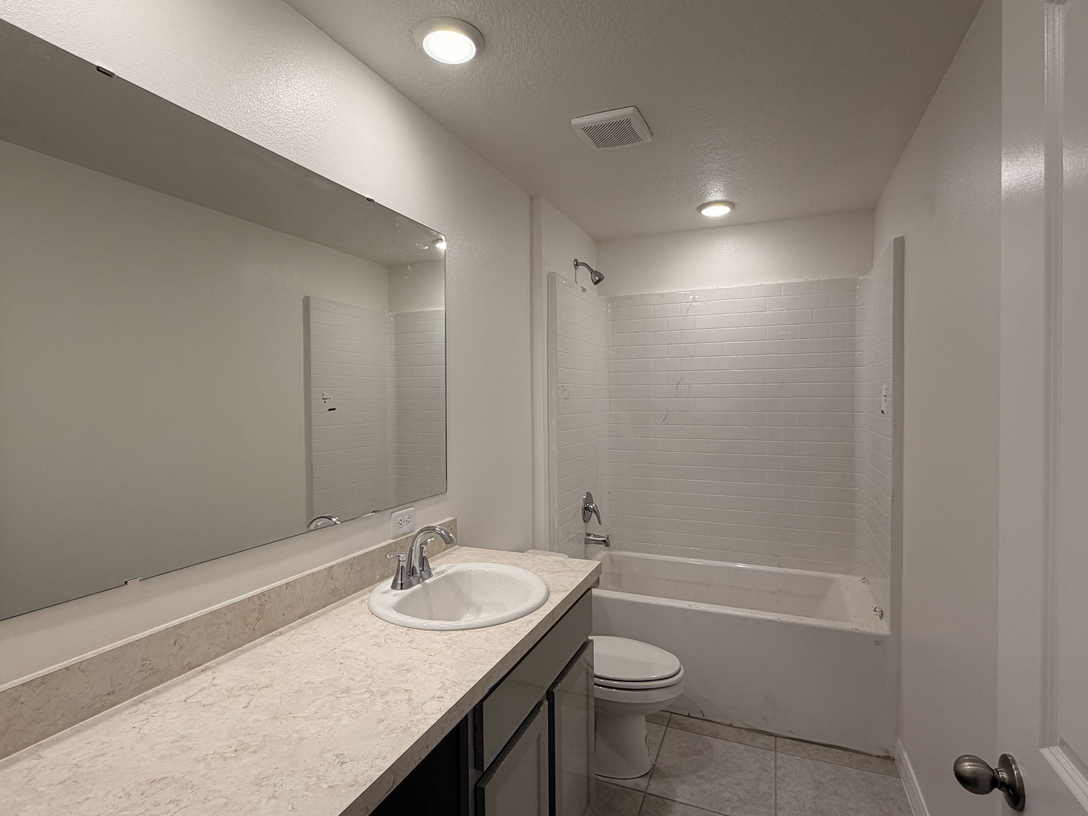 Modern bathroom featuring a white vanity countertop with sink, large mirror, and tub with tiled shower walls.