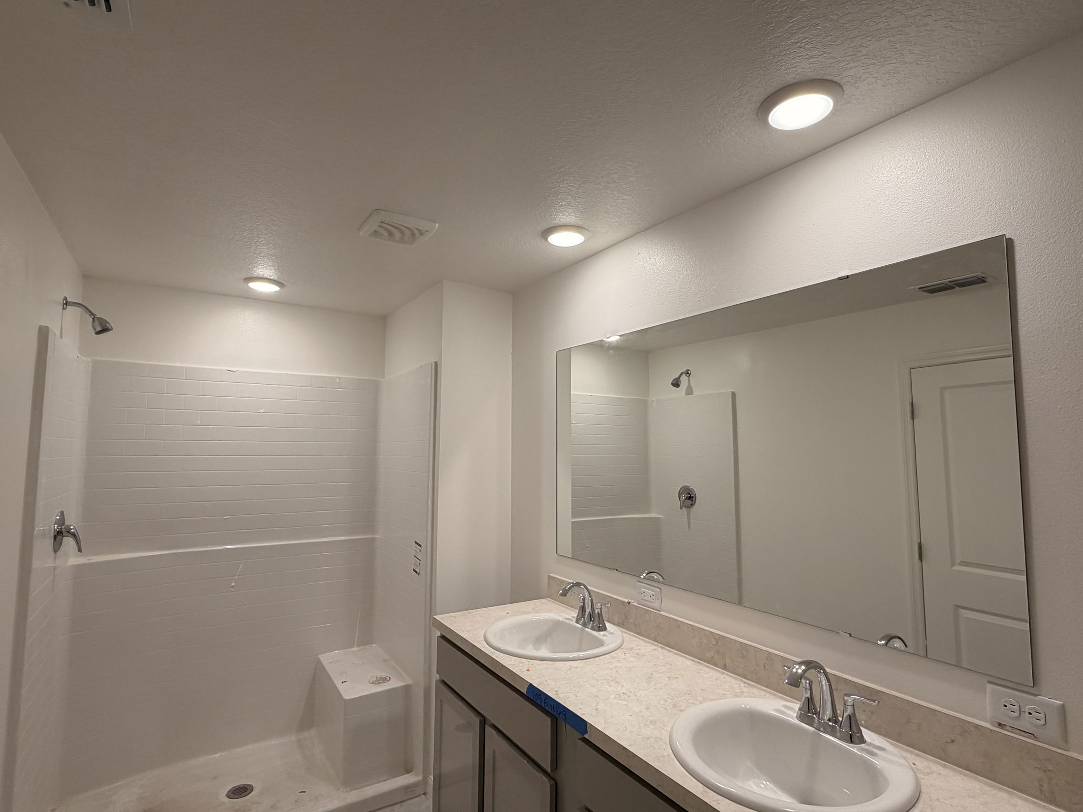Modern bathroom with dual sinks, large wall mirror, and a spacious walk-in shower.