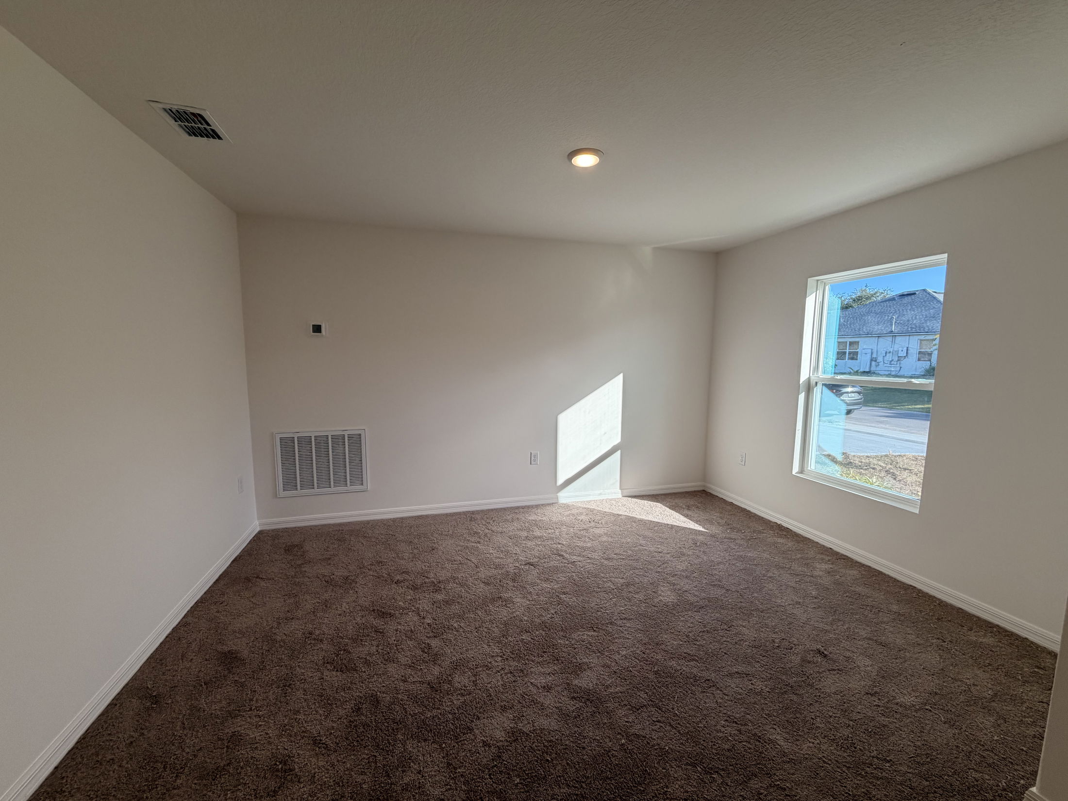 Empty room with beige walls, brown carpet, and a single window letting in natural light.
