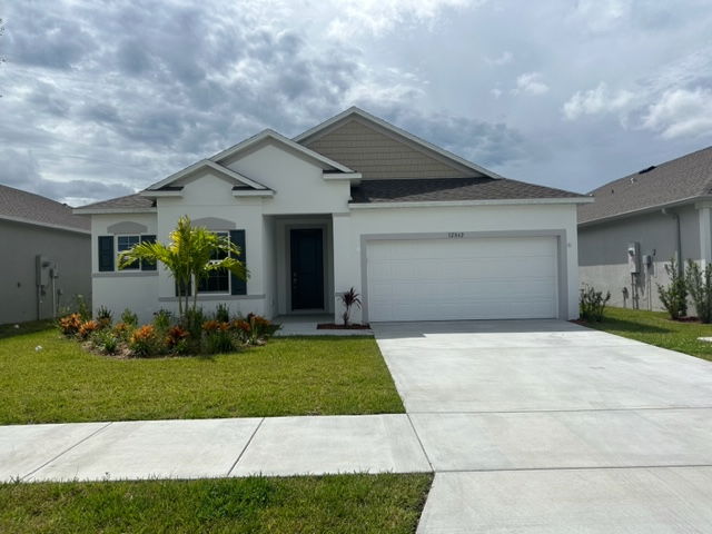 Single-story suburban home with a white facade, grey roof, and landscaped front yard, under a cloudy sky.