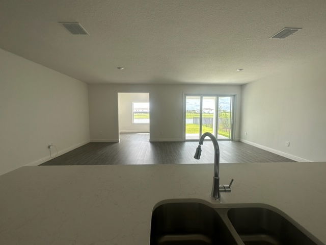 Modern open-plan living room with large windows and a view of the backyard, seen from a kitchen sink countertop.