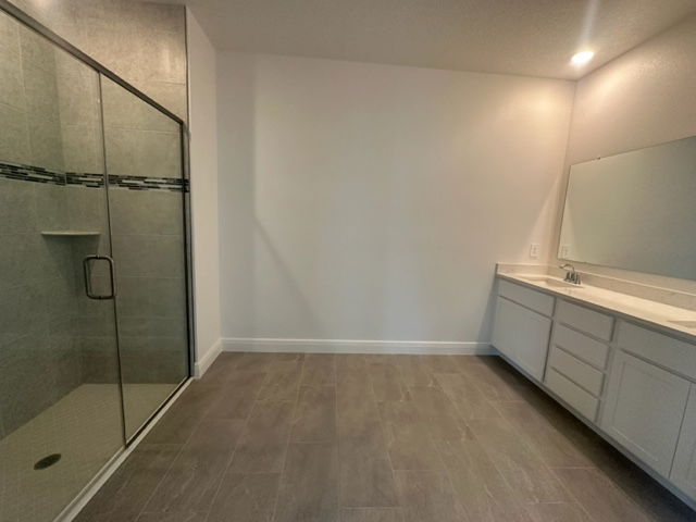 Modern bathroom with glass shower door, large mirror, and white cabinetry on gray tiled floor.