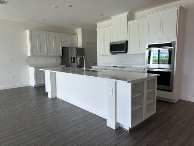 Modern kitchen with white cabinetry, stainless steel appliances, and a large central island on sleek gray flooring.