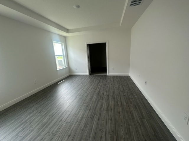Spacious modern room with gray hardwood flooring, white walls, and a single window providing natural light.