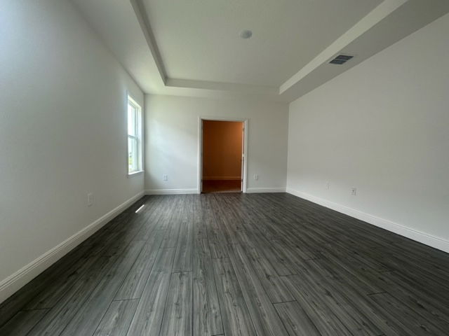 Modern empty room with gray hardwood flooring, white walls, and large window for natural light.