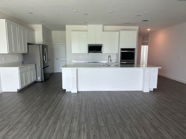Modern kitchen with white cabinetry, stainless steel appliances, and a spacious island on dark wood flooring.