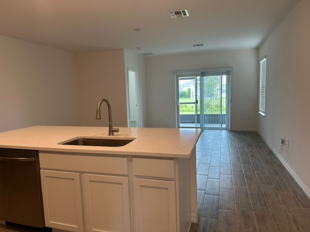 Modern open-concept kitchen and living area with a sleek faucet, white cabinetry, tiled floors, and natural light from glass doors.