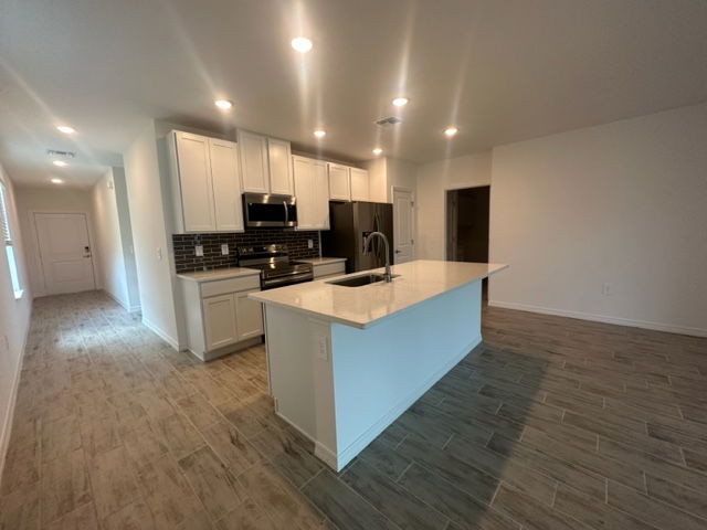 Modern kitchen interior with white cabinets, large island, and stainless steel appliances in an open-concept layout.