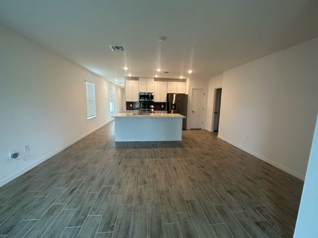 Open-concept modern kitchen with white cabinets, stainless steel appliances, and wood-style tile flooring.