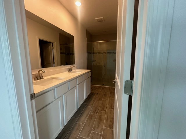 Modern bathroom with dual sinks, wooden floor tiles, large mirror, and glass-door shower.