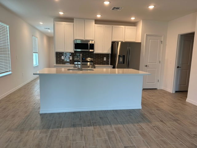 Modern kitchen with white cabinetry, stainless steel appliances, and tile flooring in a spacious home interior.
