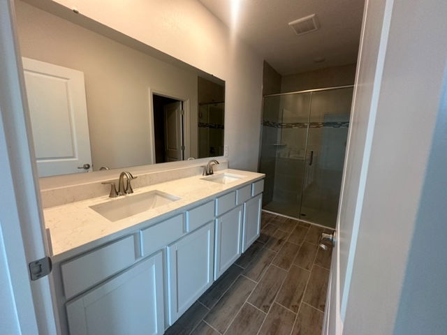 Modern bathroom interior with dual sinks, large mirror, white cabinetry, and a glass-enclosed shower.