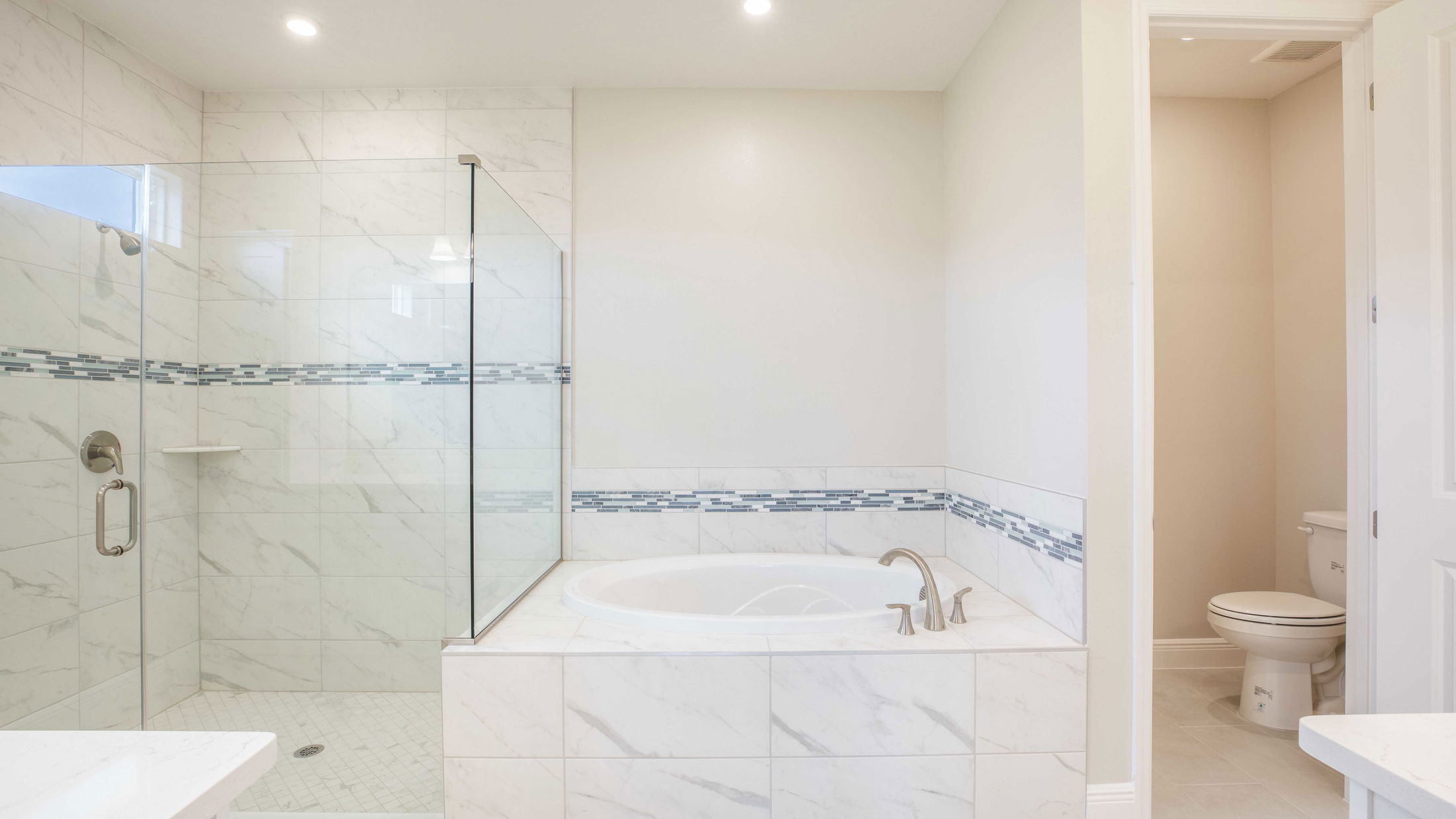 Elegant bathroom with a glass walk-in shower, white marble tiles, and built-in bathtub.