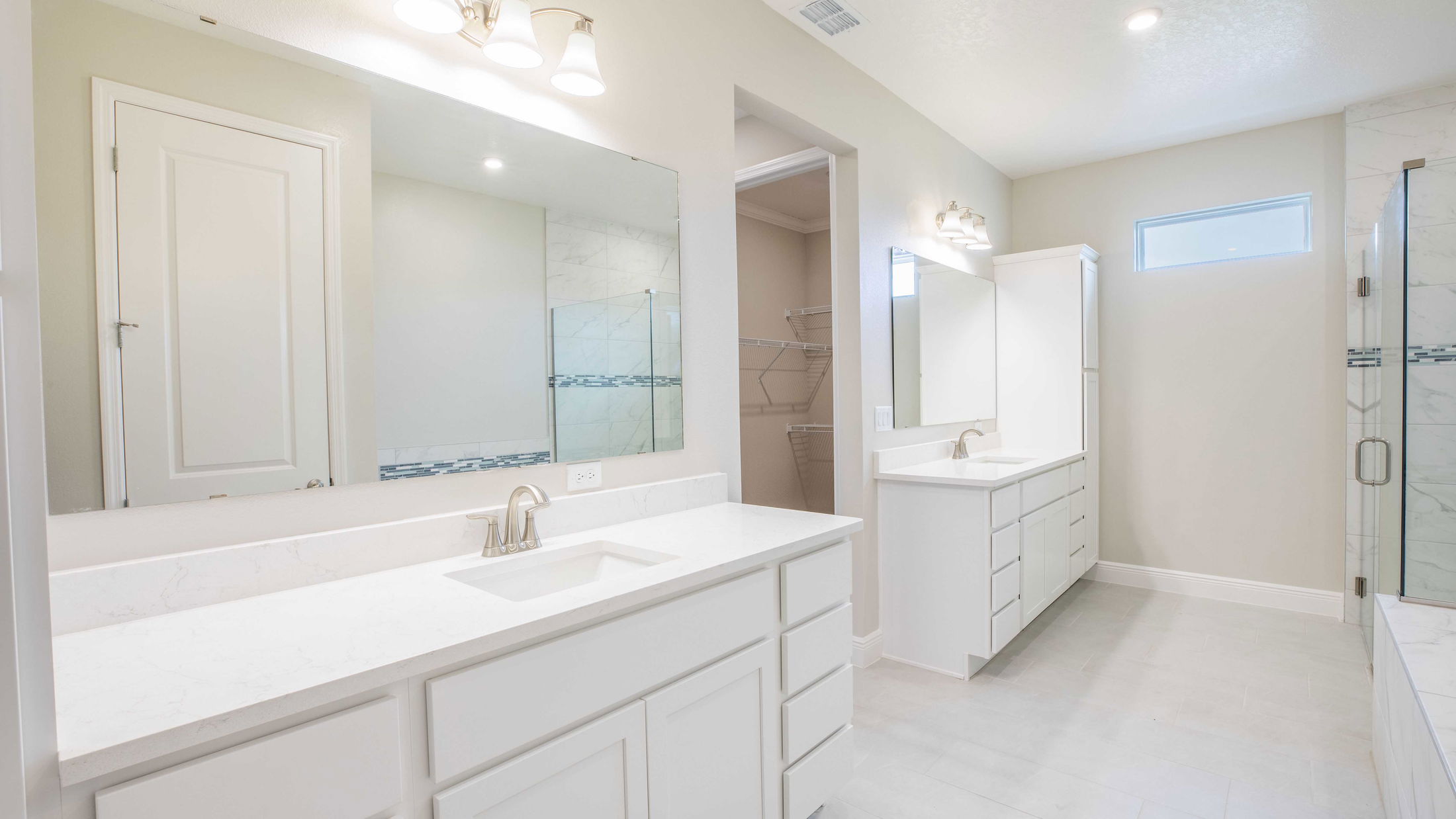 Modern bathroom with dual white vanities, large mirrors, and a glass-enclosed shower.