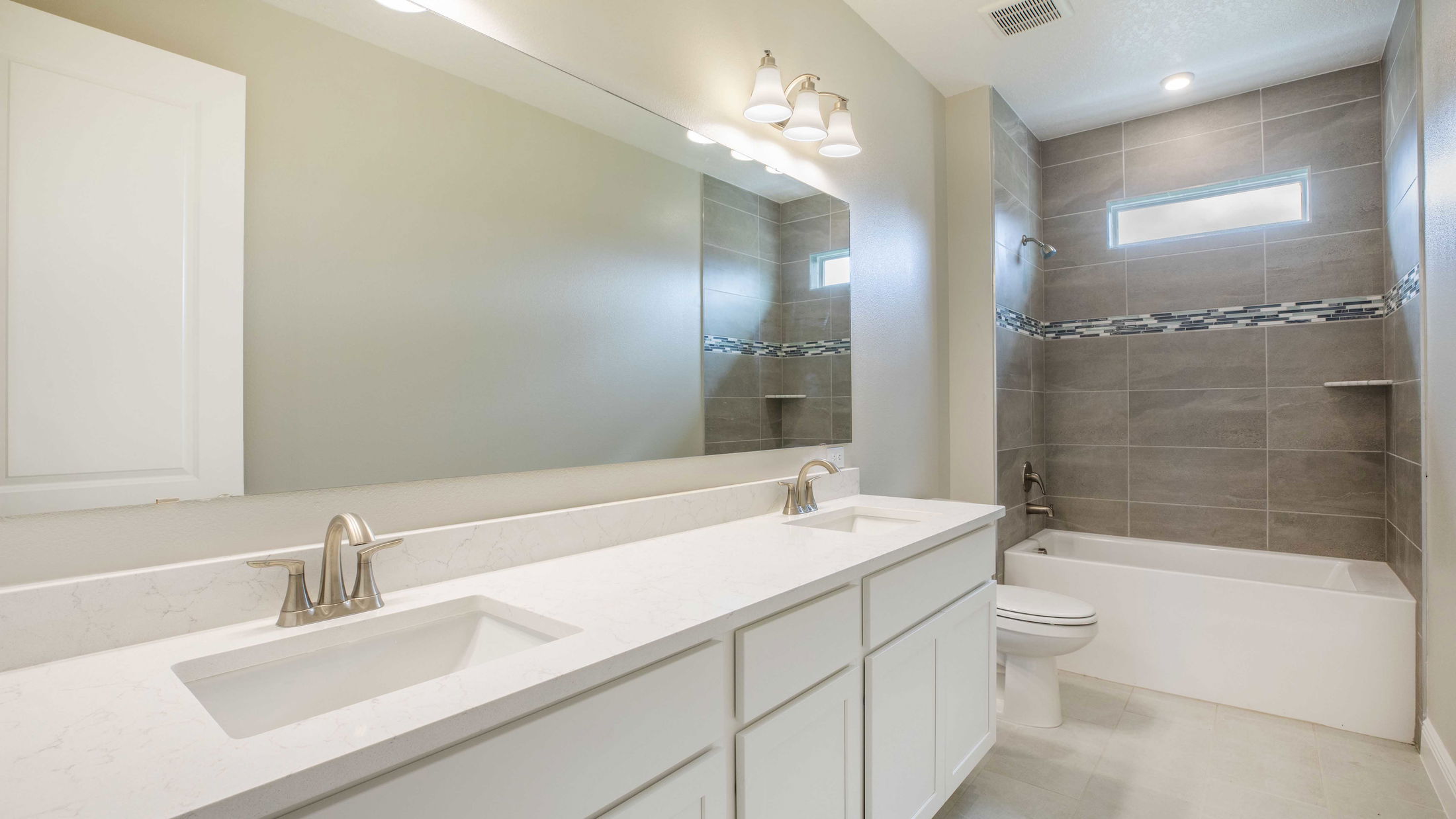 Modern bathroom with double sink vanity, elegant lighting, and tiled shower area.