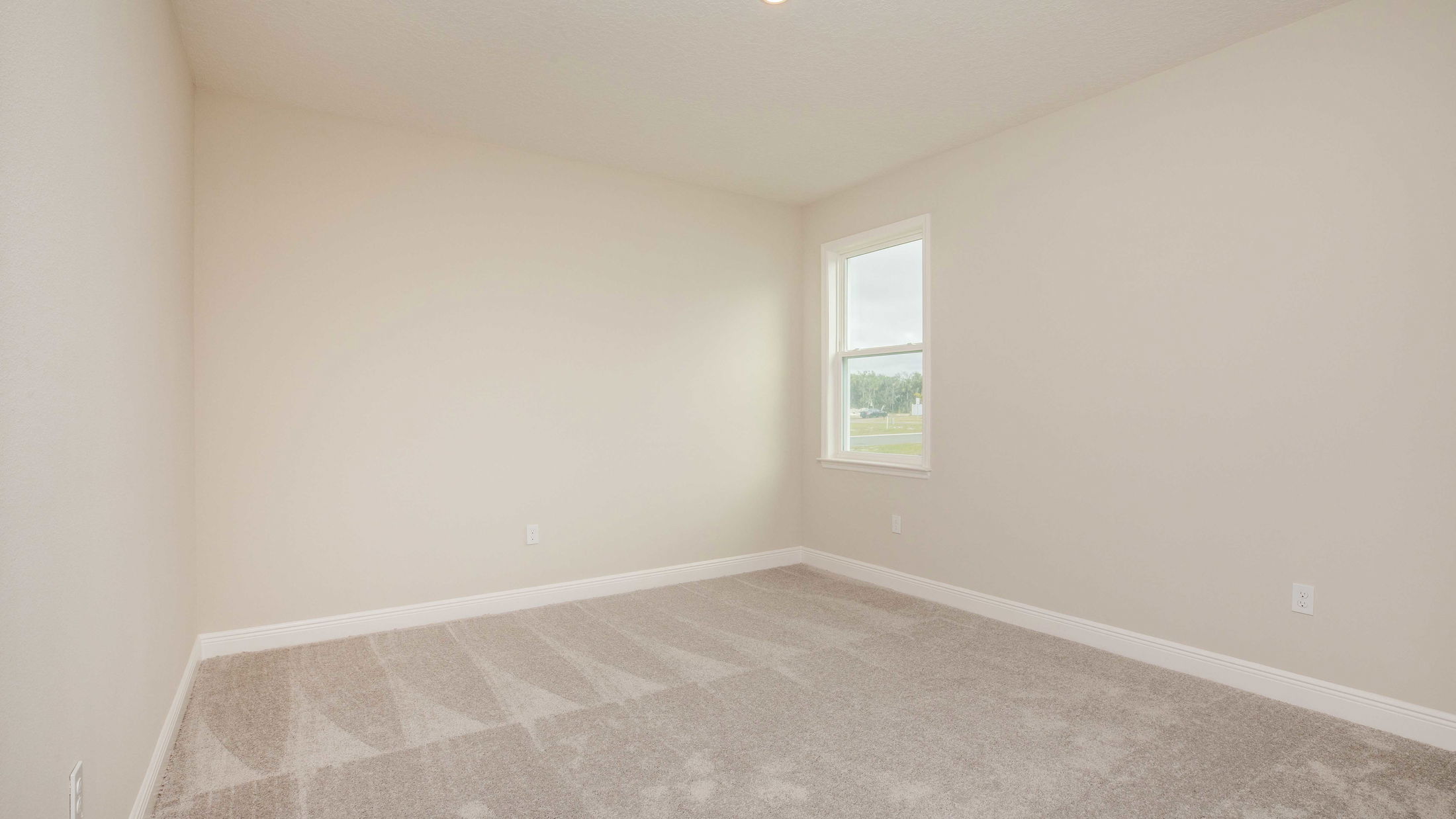 Empty beige room with clean carpeting and a single window, perfect for home staging or real estate showcase.