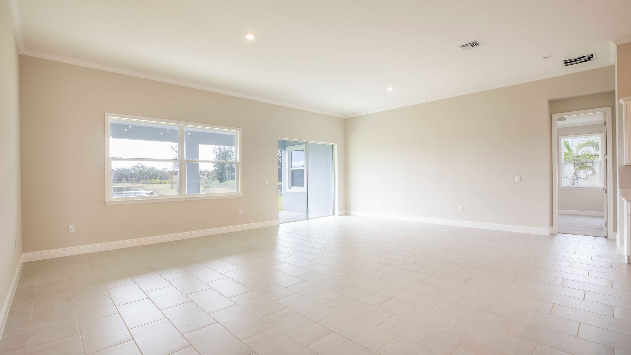Spacious, empty living room with beige tiled floor, large windows, and sliding glass door overlooking a scenic landscape.