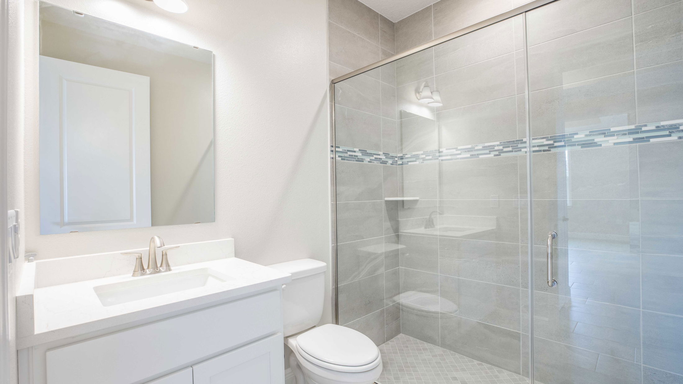 Modern bathroom with glass shower enclosure, tiled walls, and a sleek white vanity.