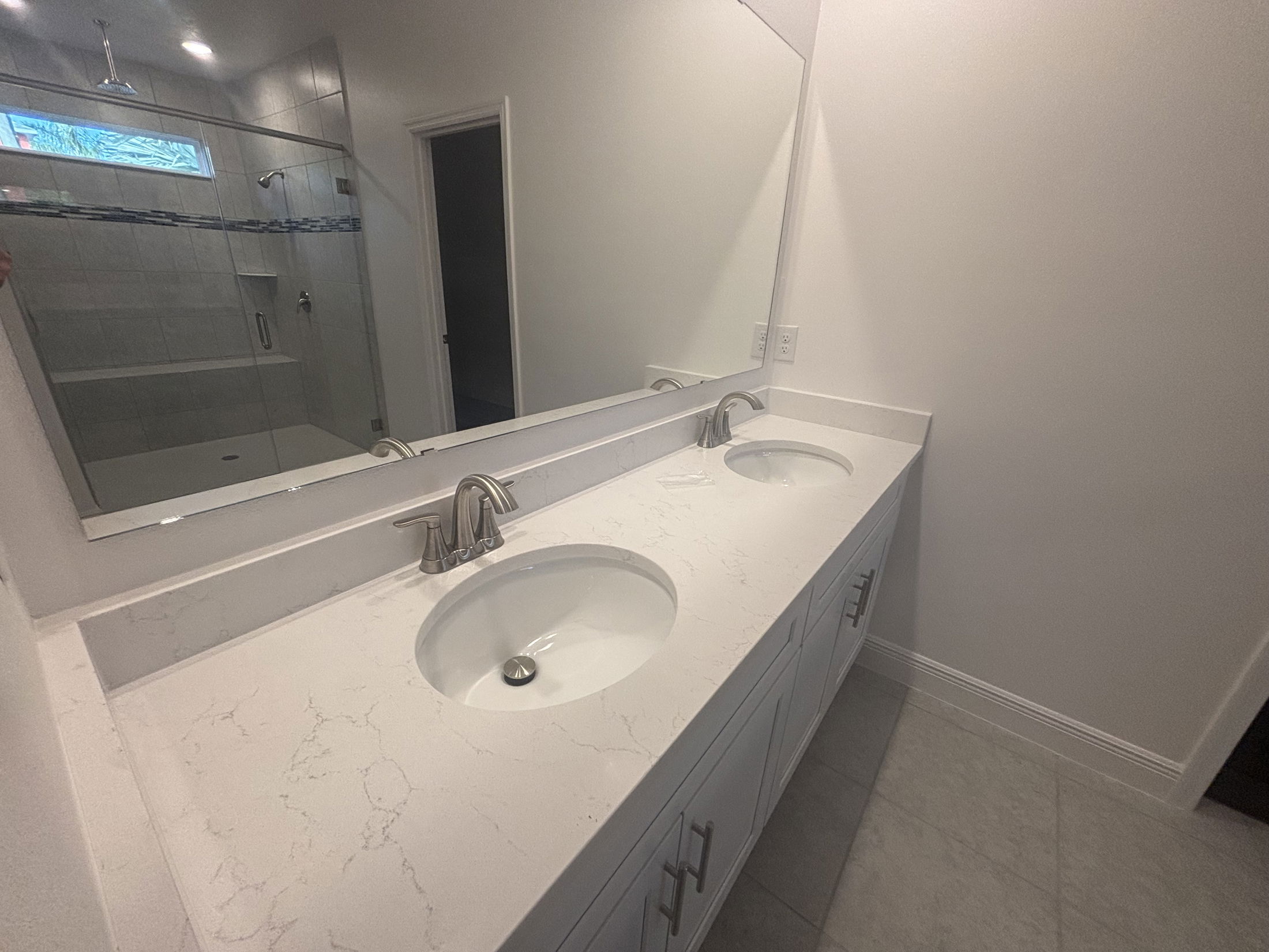 Modern bathroom with a spacious double sink vanity, marble countertop, large mirror, and a glass-enclosed shower.