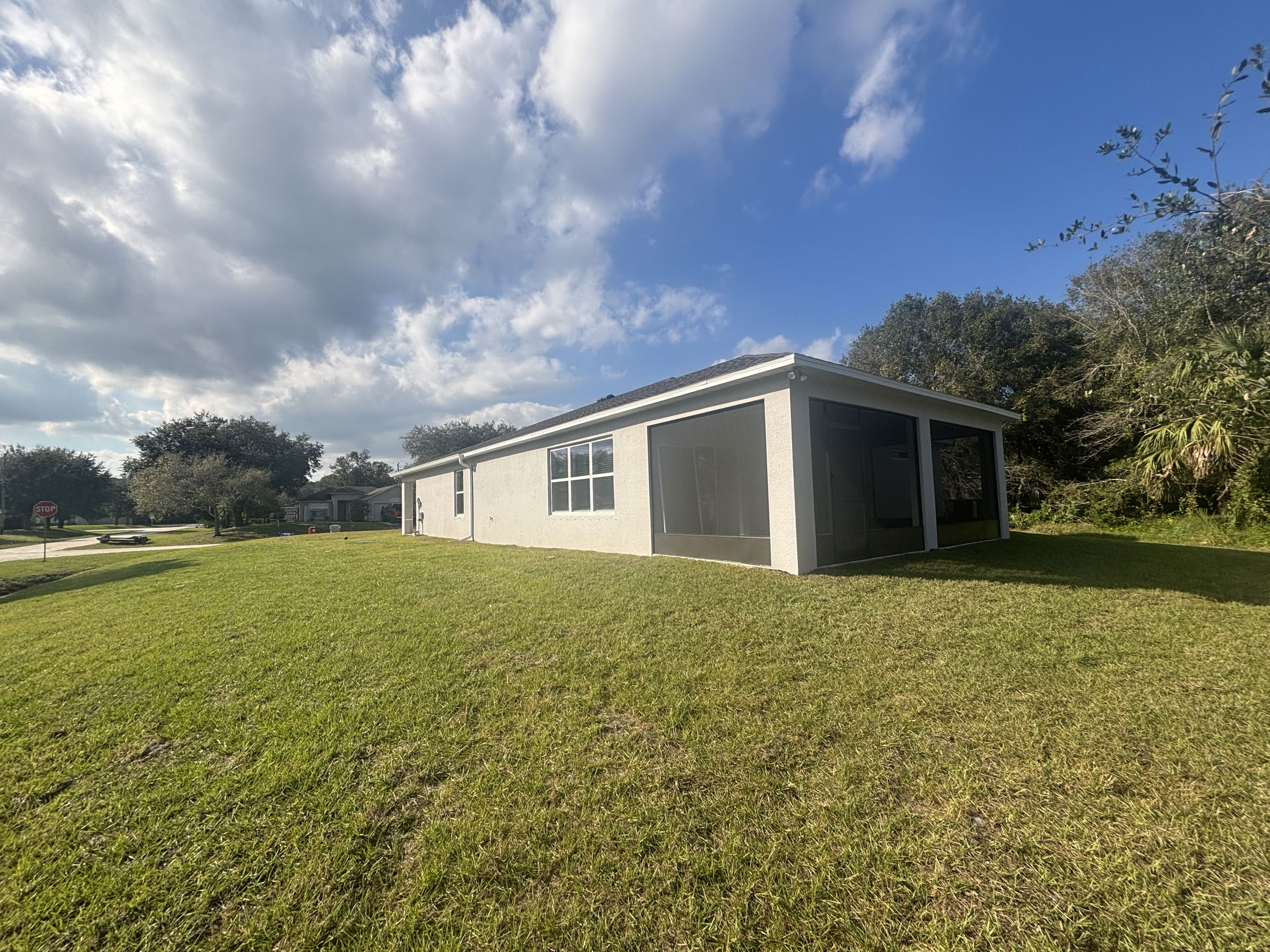 A modern white house with a spacious green lawn and clear sky in a suburban neighborhood setting.