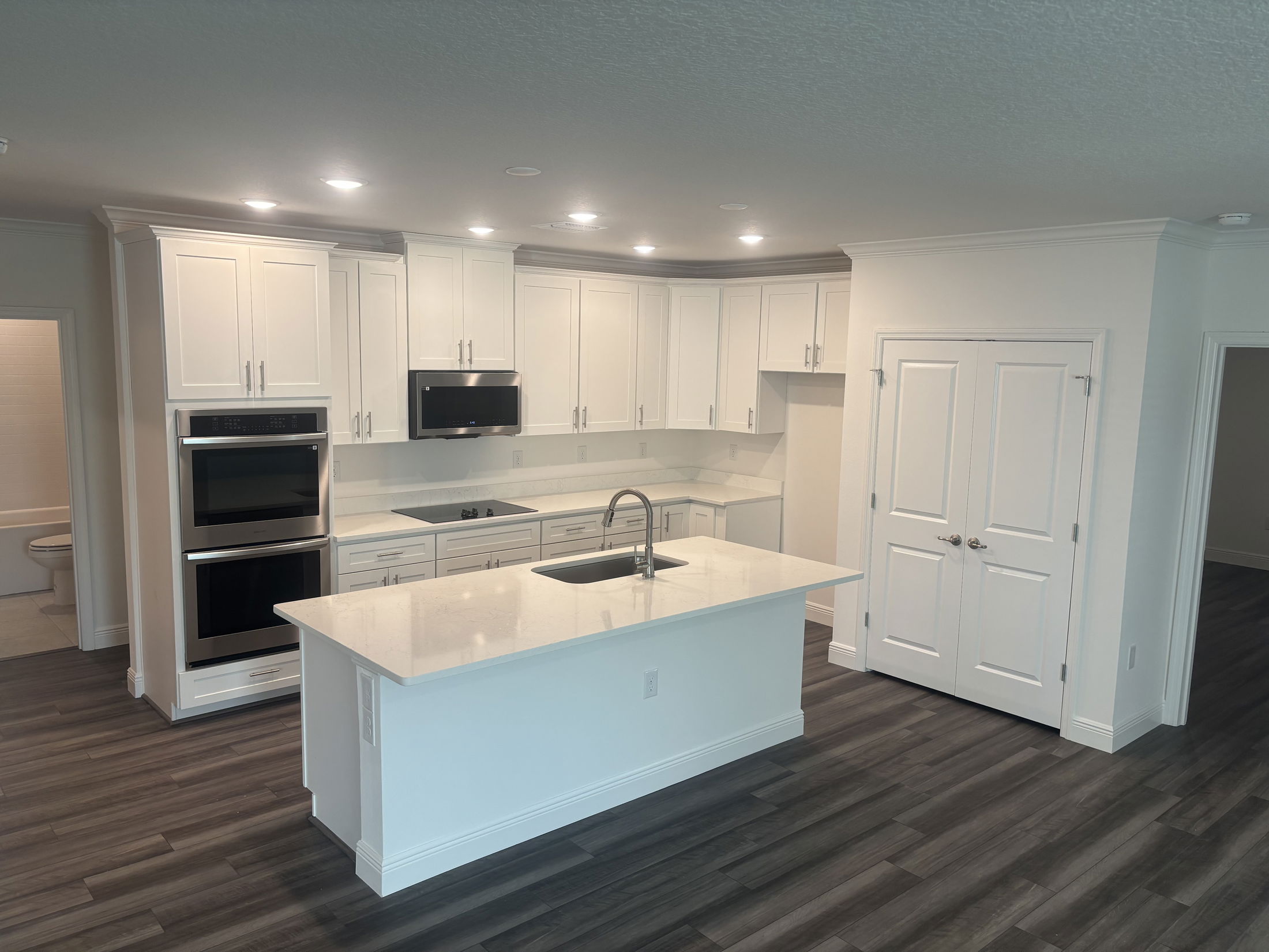 Modern kitchen with white cabinets, stainless steel appliances, and a central island with a sink on dark wood flooring.
