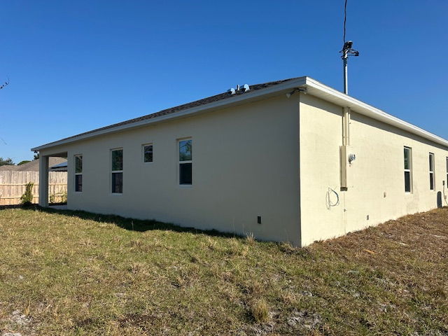 Single-story beige house with multiple windows, situated in a grassy backyard under a clear blue sky.