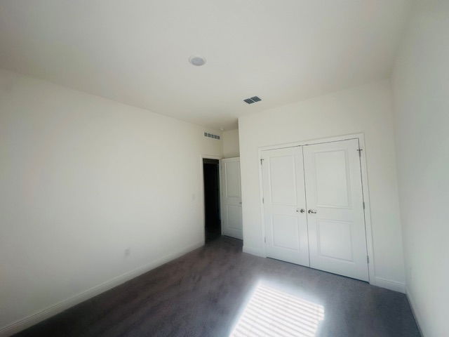 Empty white-walled room with carpet, double doors, and natural light streaming through a window.
