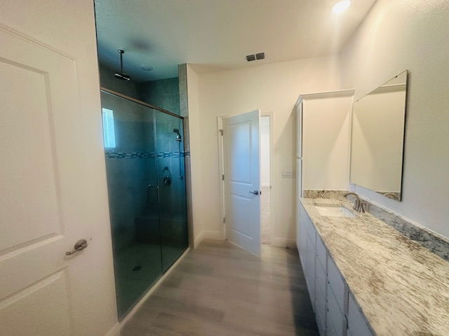Modern bathroom with glass shower, marble countertop, and double sinks on a light wood floor.