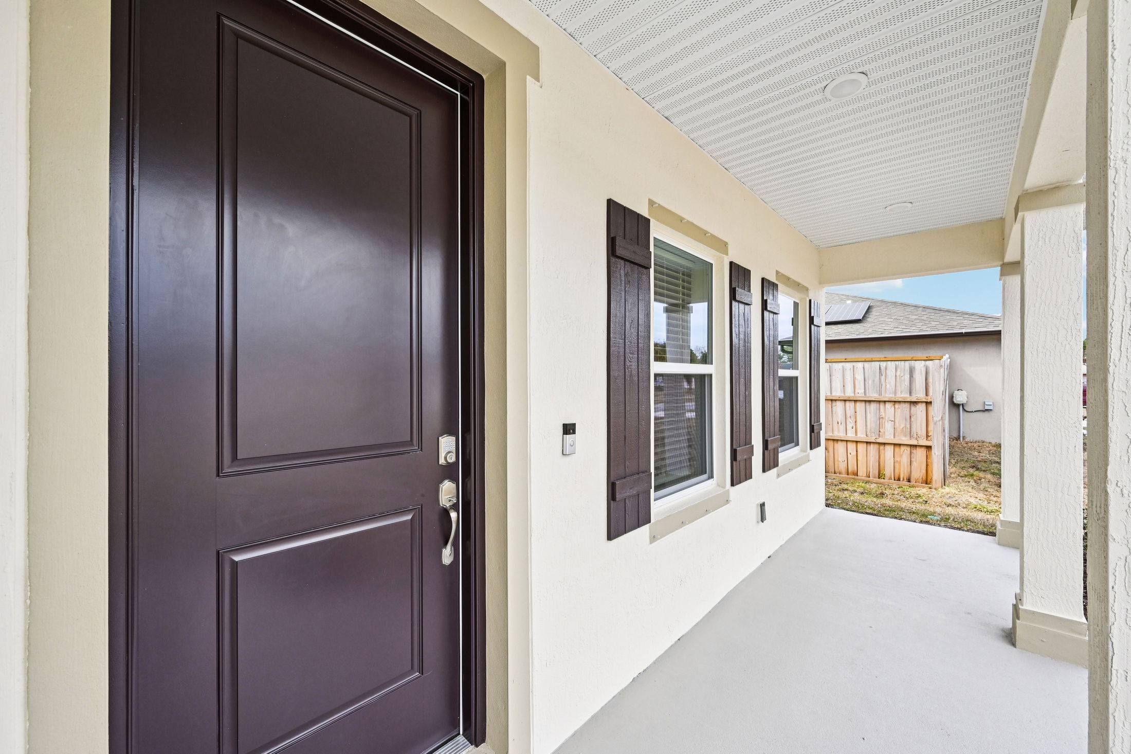 Exterior view of a modern home entrance featuring a dark wooden door, decorative shutters on windows, and a covered porch area.