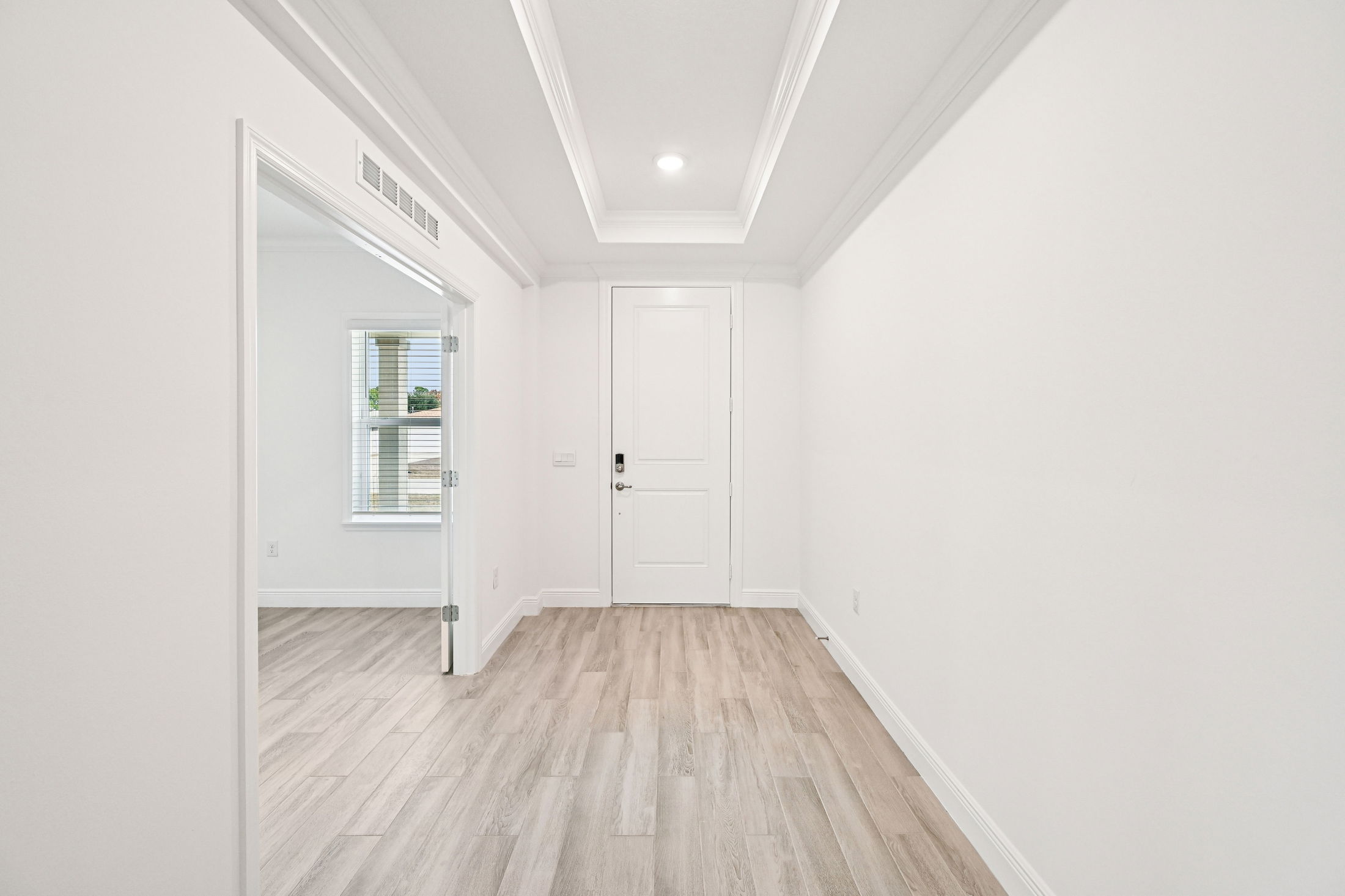 Bright and airy entryway featuring light wood flooring and white walls with decorative molding.