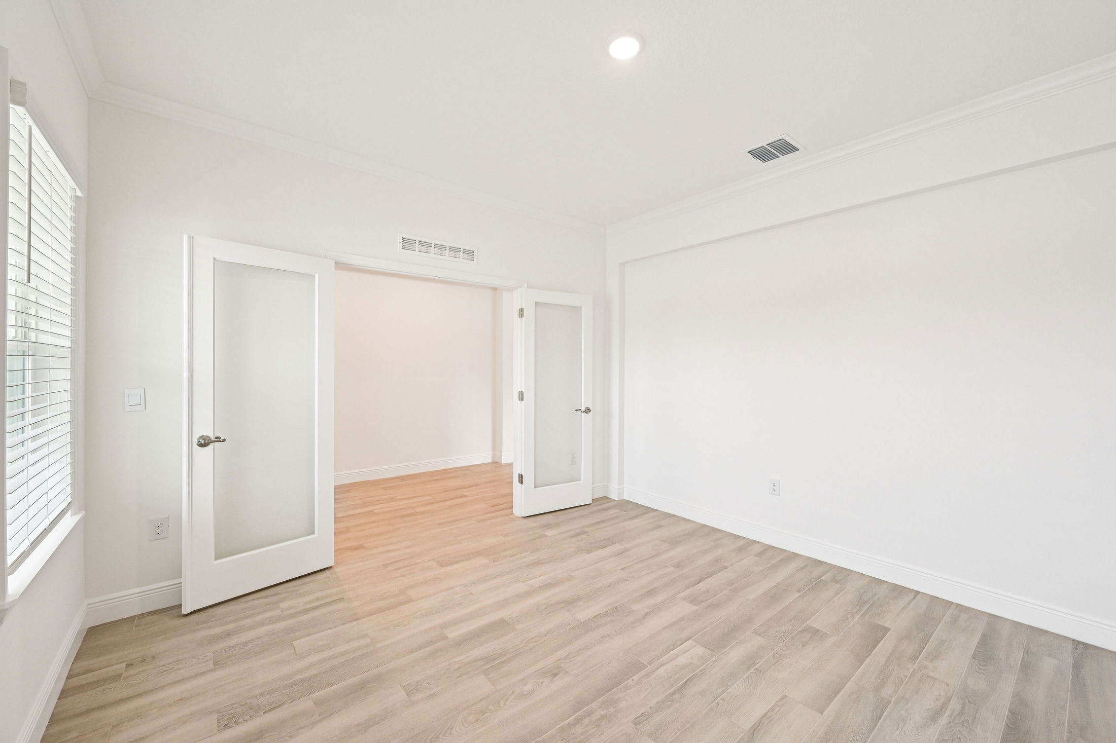 Bright and airy empty room with light wood flooring and glass-paneled doors, ideal for a home office or bedroom setup.