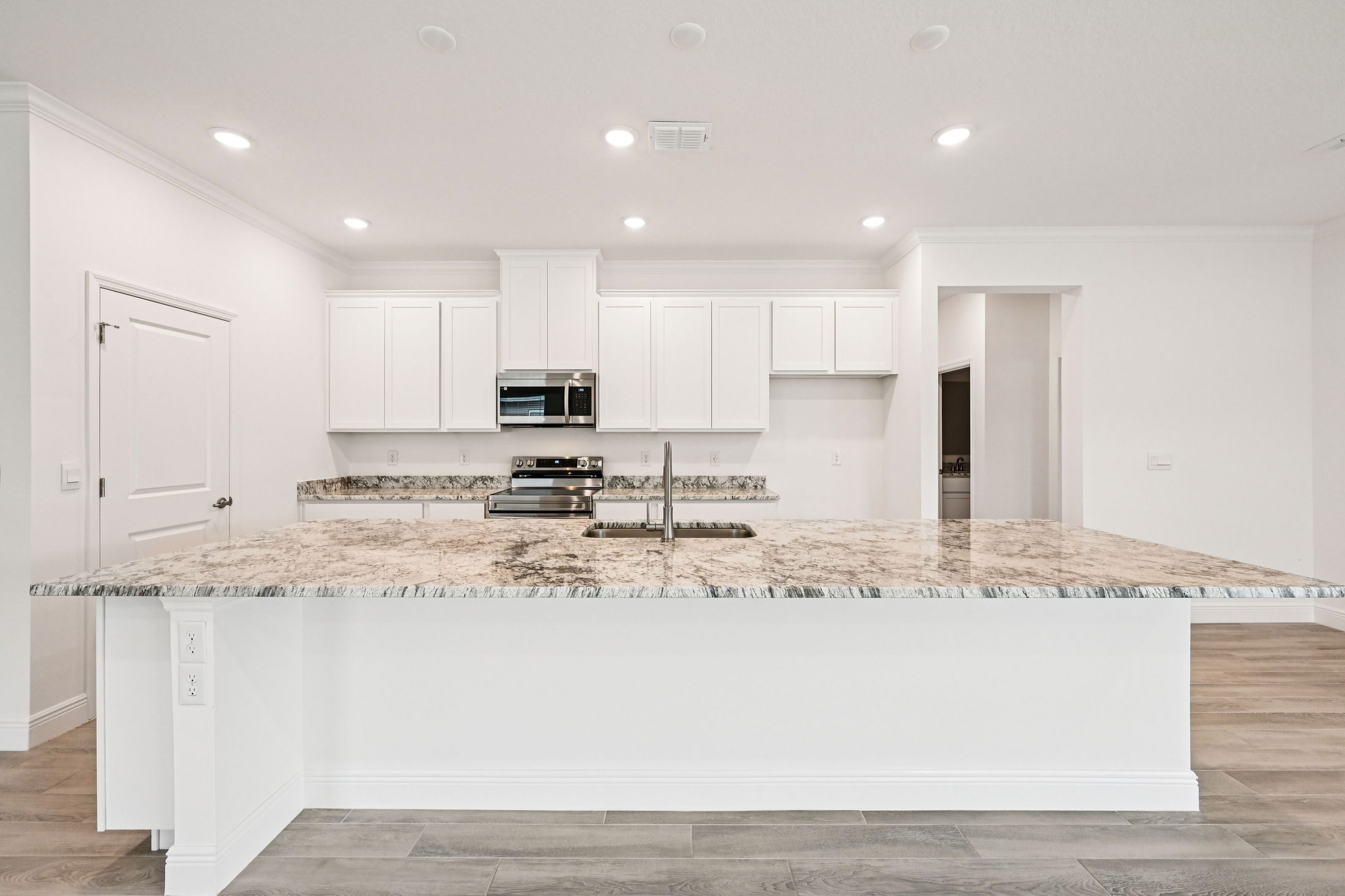 Modern kitchen interior featuring white cabinets, stainless steel appliances, and a large granite countertop.