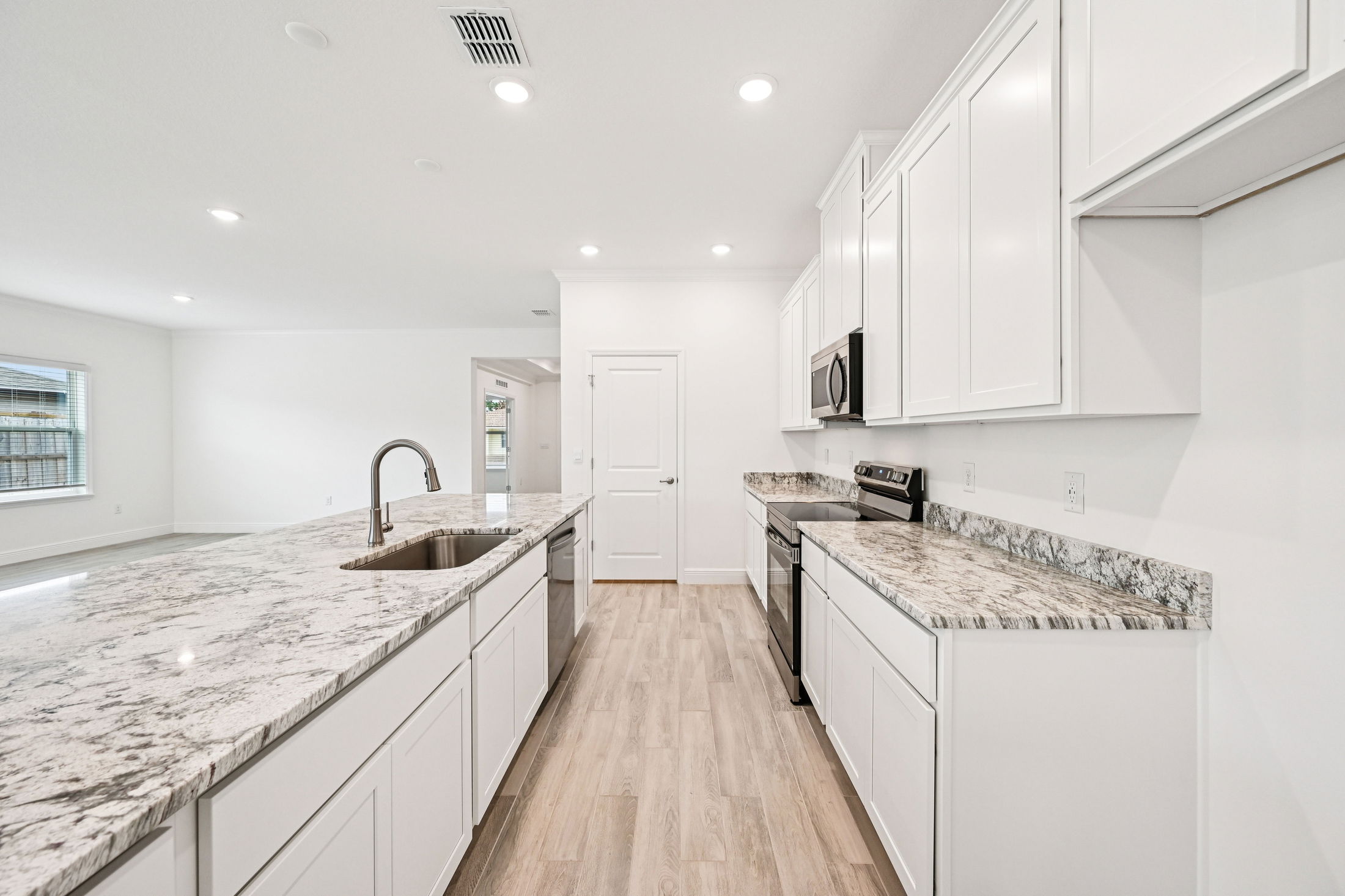 Modern kitchen featuring white cabinets, granite countertops, stainless steel appliances, and a spacious layout with natural lighting.