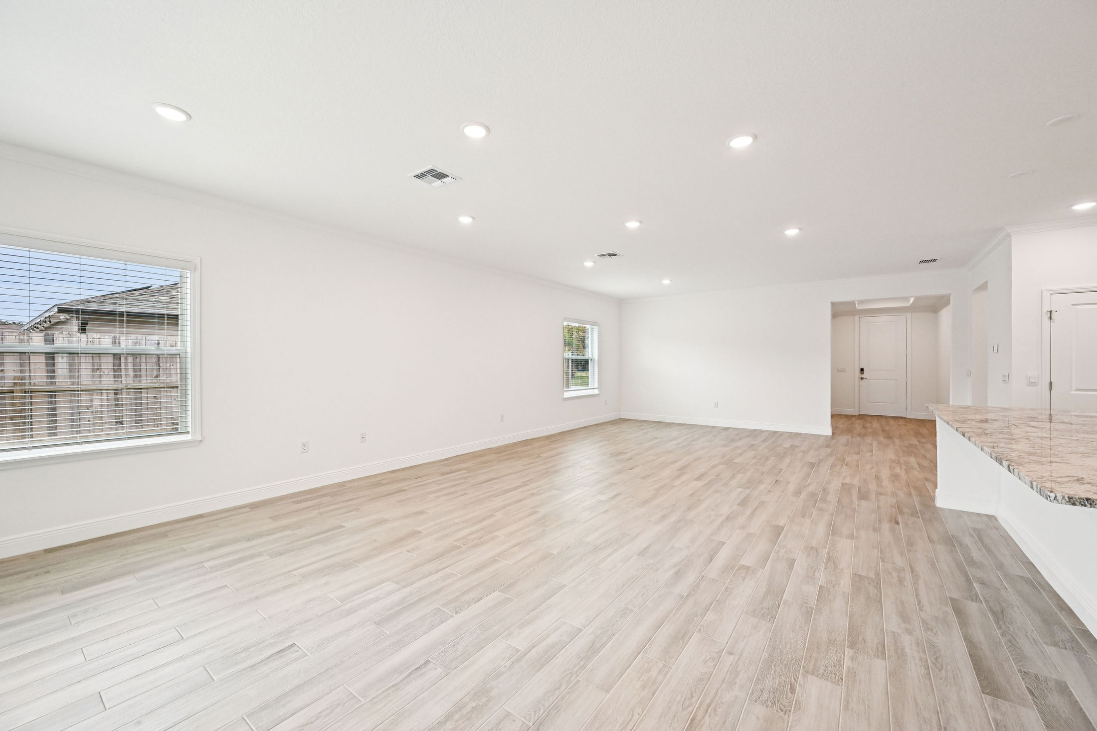 Spacious modern living room with light wood flooring and ample natural light from large windows.