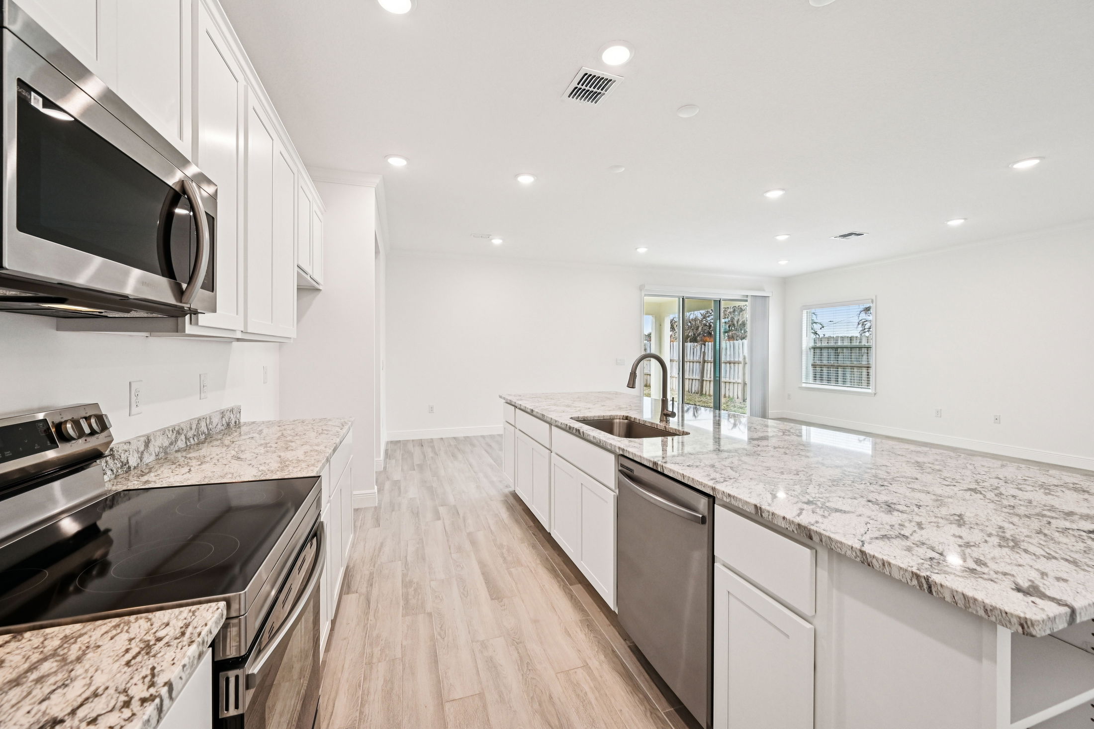 Modern kitchen featuring stainless steel appliances, granite countertops, and white cabinetry with ample natural light.