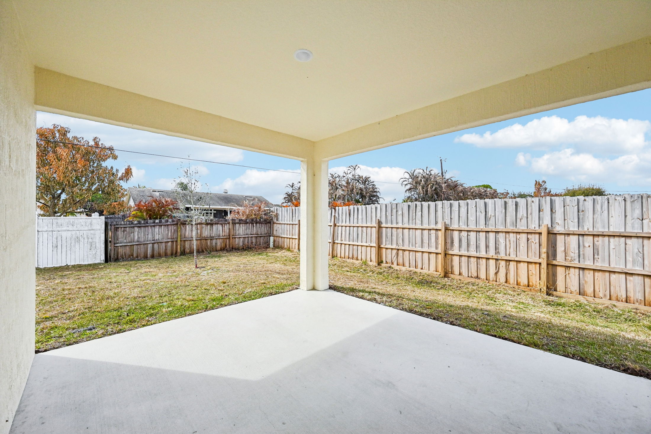 Spacious patio view overlooking a fenced backyard with green grass and cloudy blue sky.