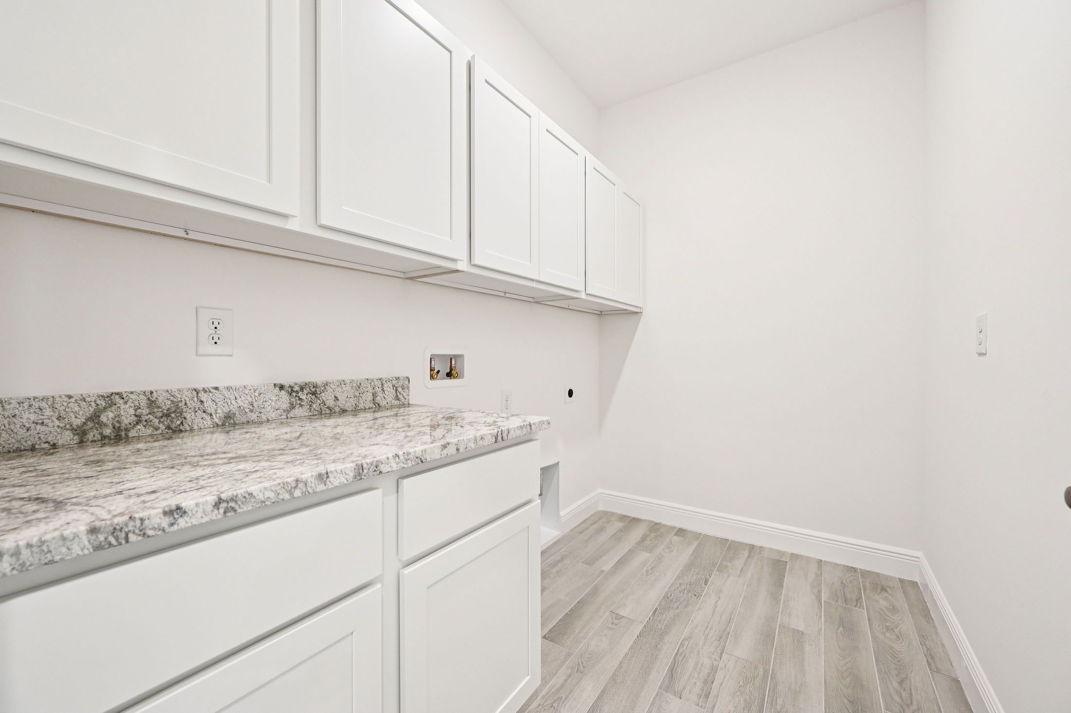 Modern laundry room featuring white cabinets, a granite countertop, and light wood flooring.