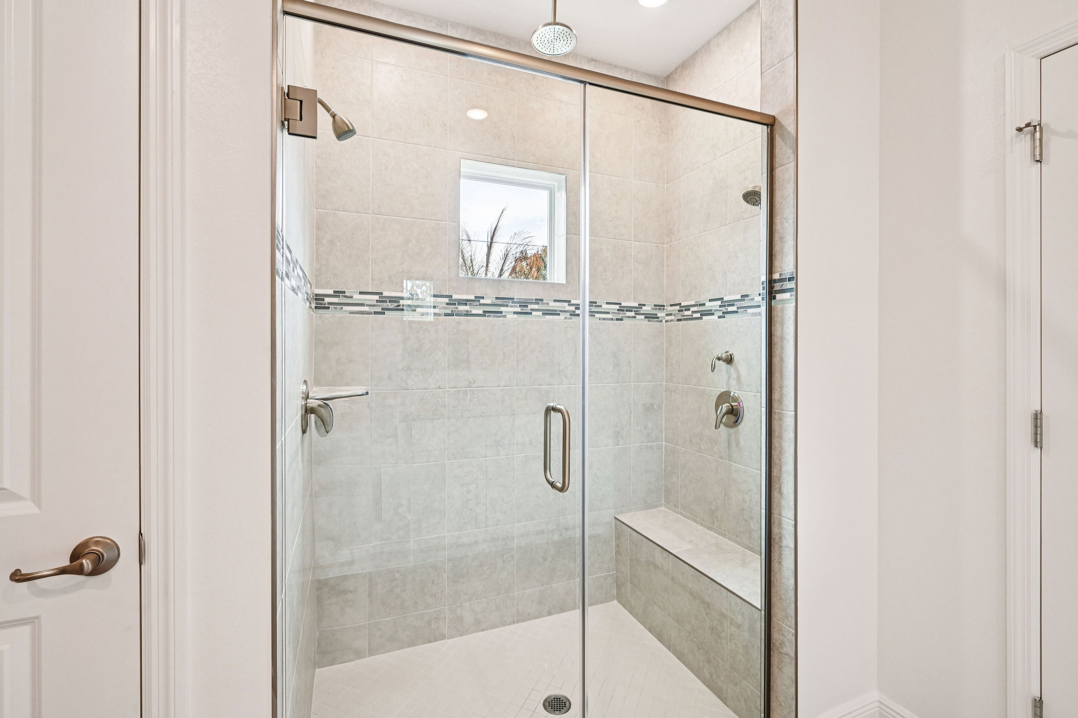 Modern glass shower with tile design and built-in seating in a bright bathroom.