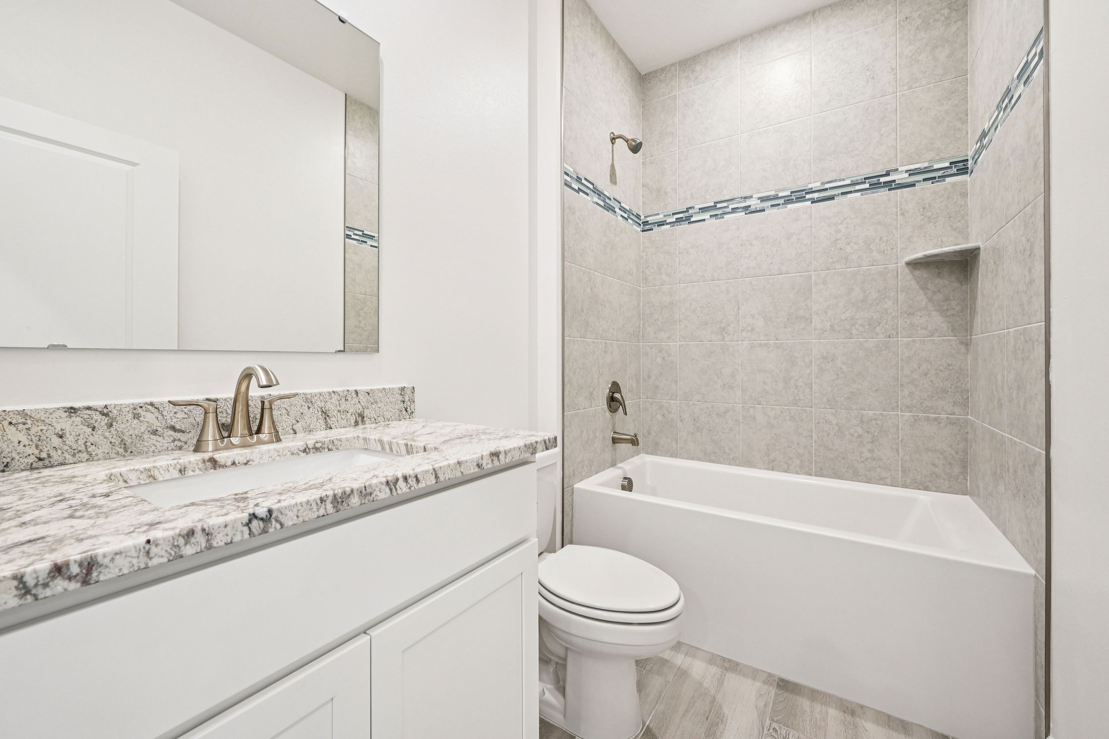 Modern bathroom with a granite countertop, white cabinetry, and a neutral tile shower area.