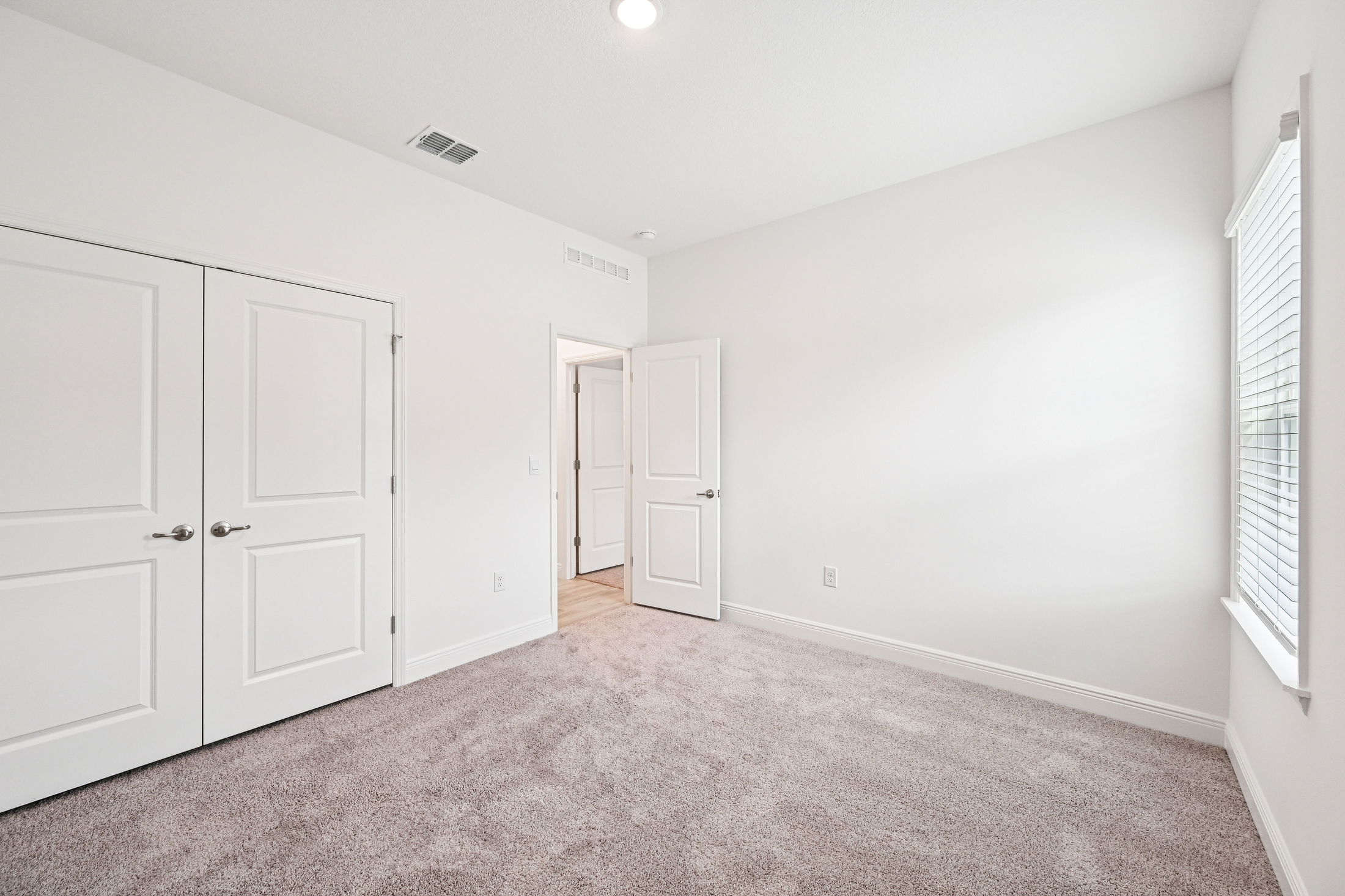 Bright, modern bedroom with light carpet, white walls, and open doors leading to adjoining rooms.